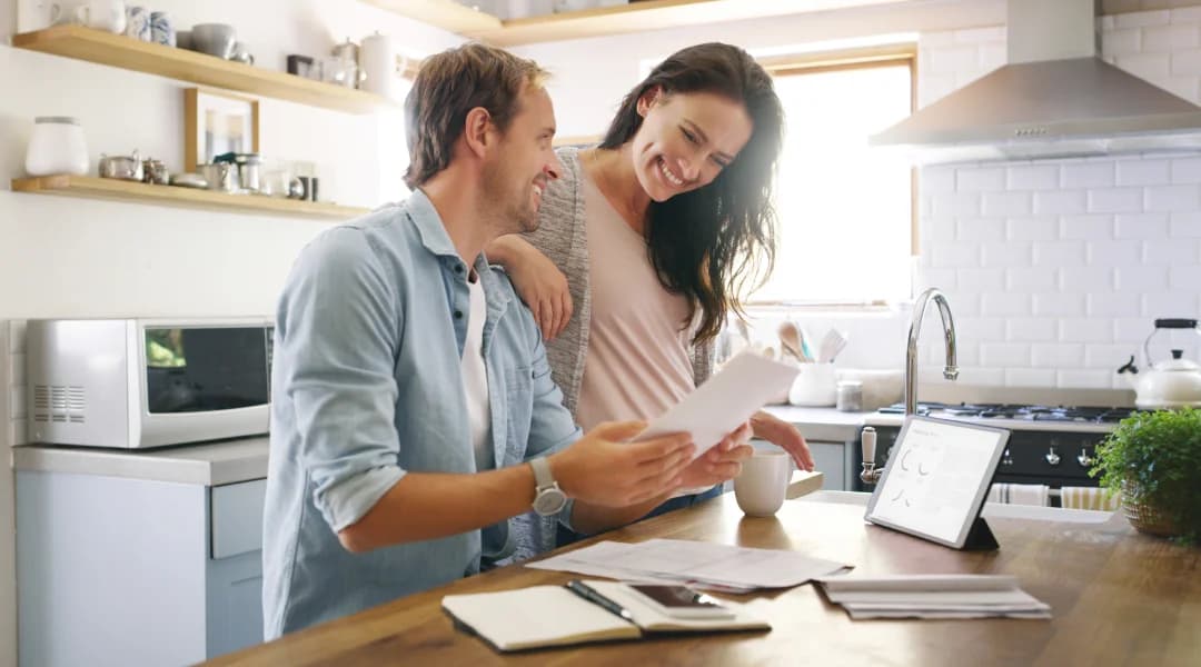 A man and woman review paperwork in a kitchen, discussing important details related to their credit score.