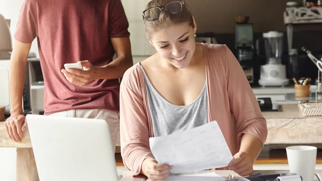 A woman and man sitting at a table with a laptop and papers, discussing personal loans.