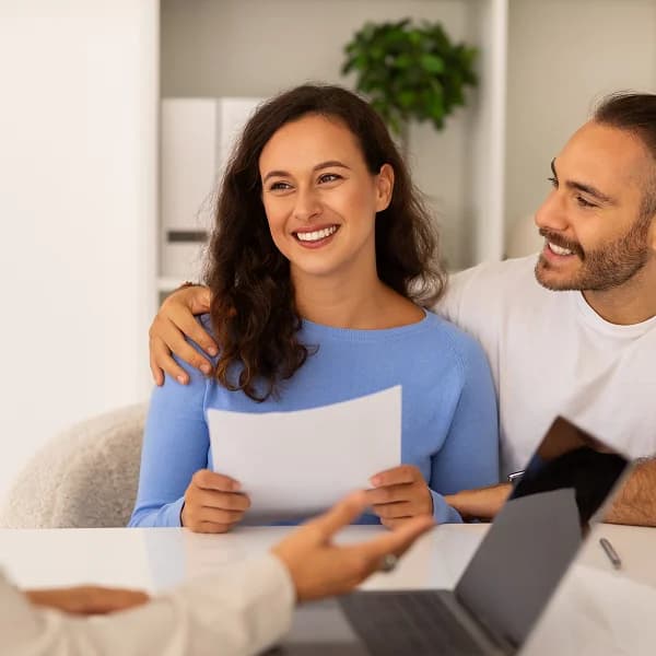 Un homme et une femme assis à une table avec un ordinateur portable et des documents, discutant d'un prêt personnel.