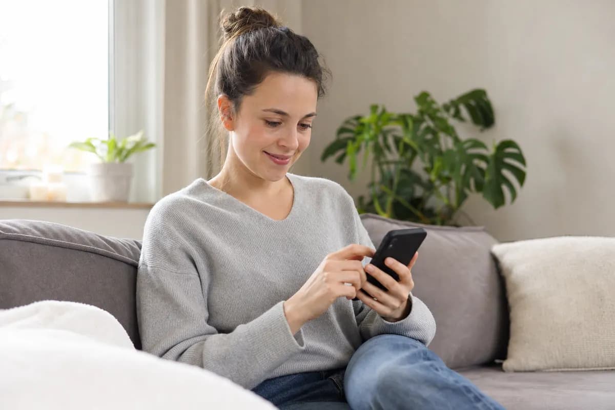 Woman on her couch applying for a small personal loan online with her smartphone