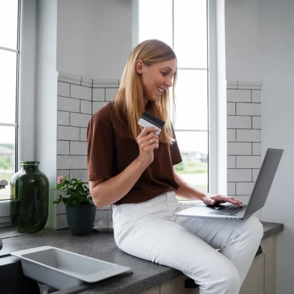 Une femme assise sur un comptoir de cuisine, utilisant un ordinateur portable et une carte de crédit, avec l'inscription prêt le jour même.
