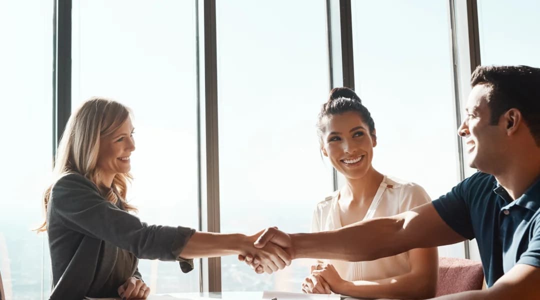 Trois professionnels se serrent la main dans un bureau, symbolisant un accord ou une collaboration réussie.