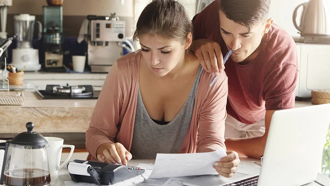 A man and woman review paperwork on a laptop, focusing on a credit file together.