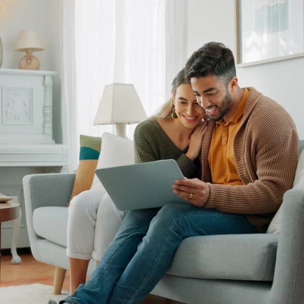 A man and woman seated on a couch, focused on a laptop, discussing options for no credit check loans.